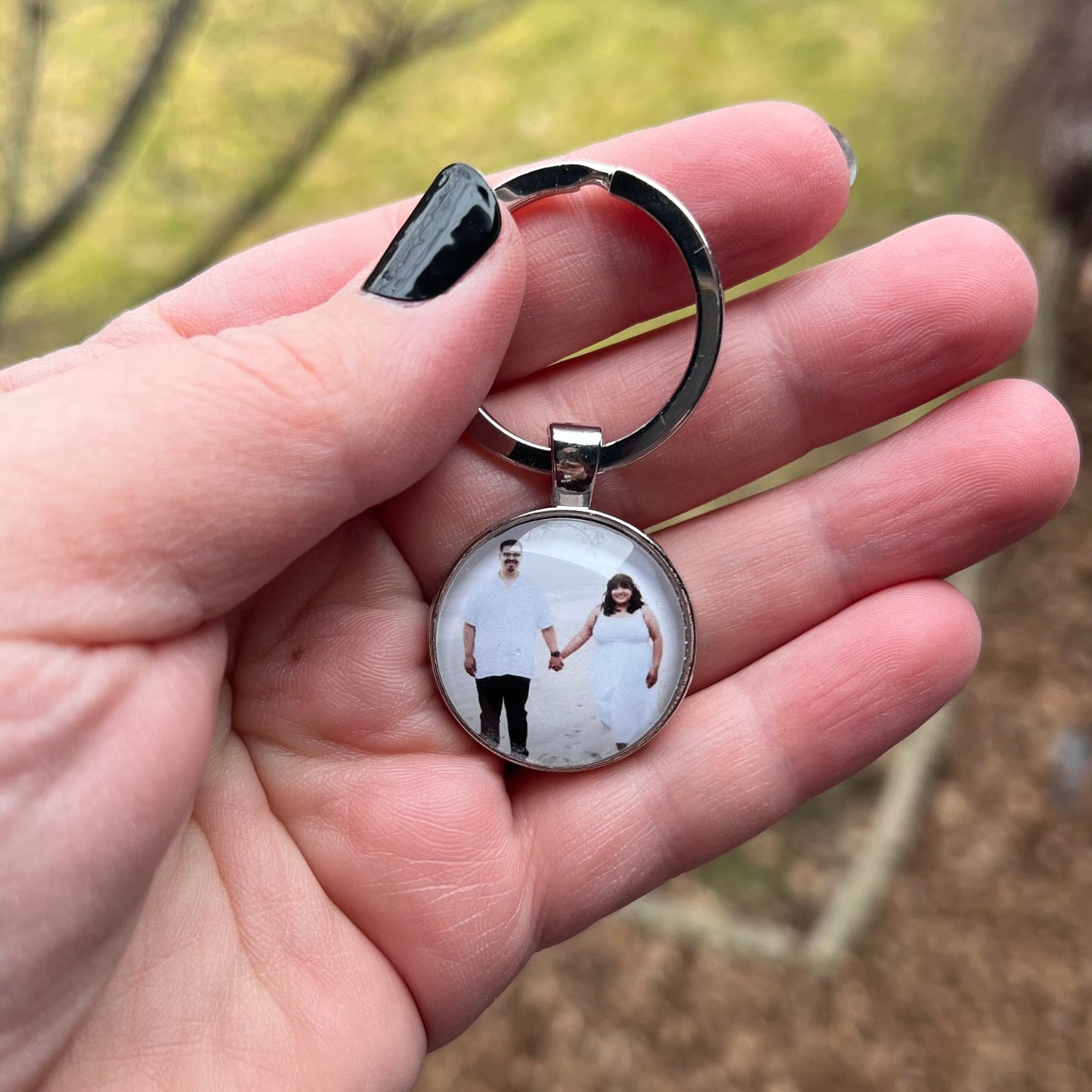 Hand holding a keychain with a photo of two people on a blurred natural background